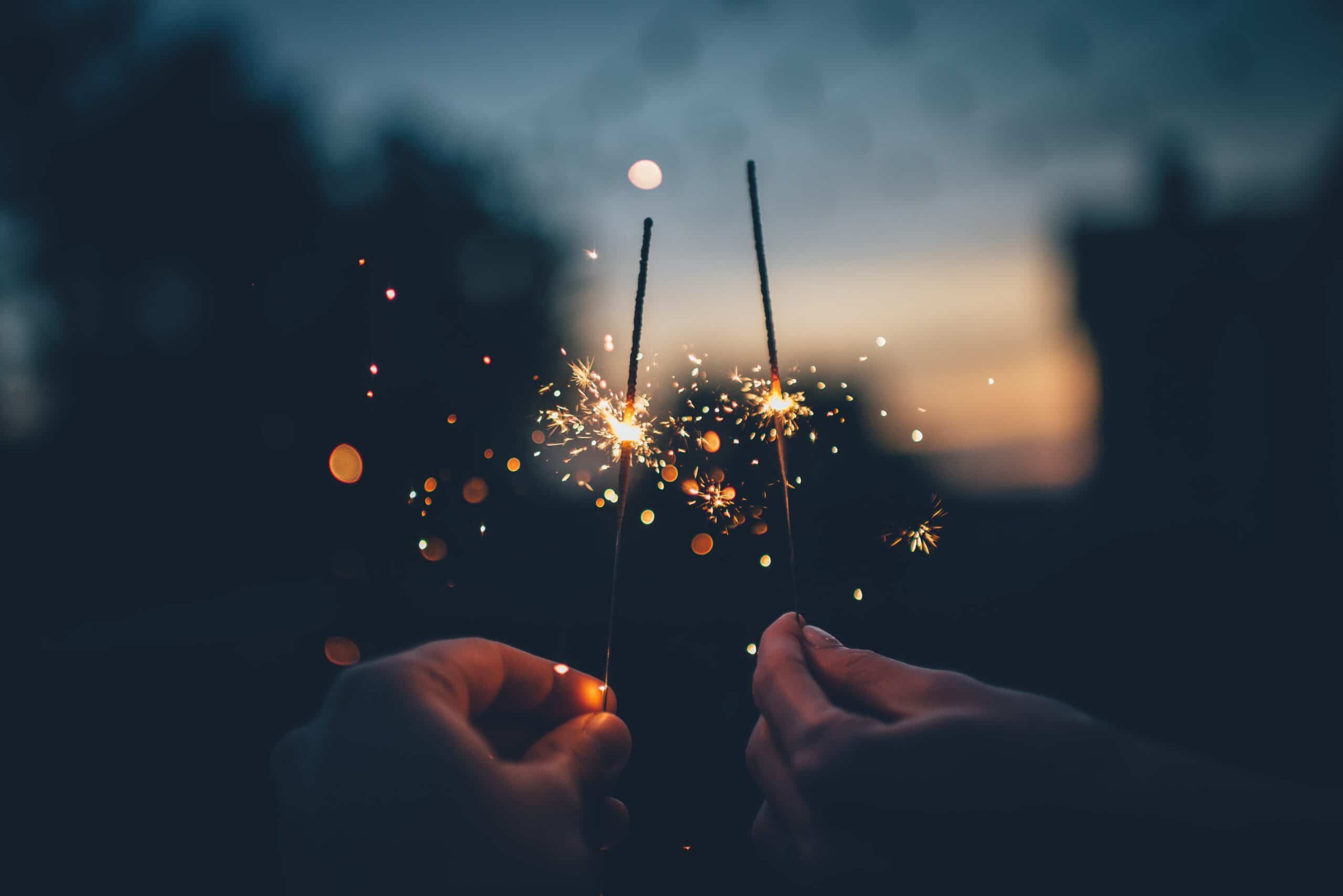 two hands holding sparklers at dusk