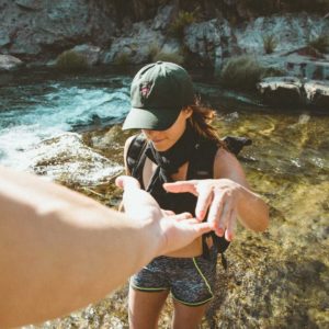 Team member Samantha in a baseball cap grabbing someone's hand as she crosses a river