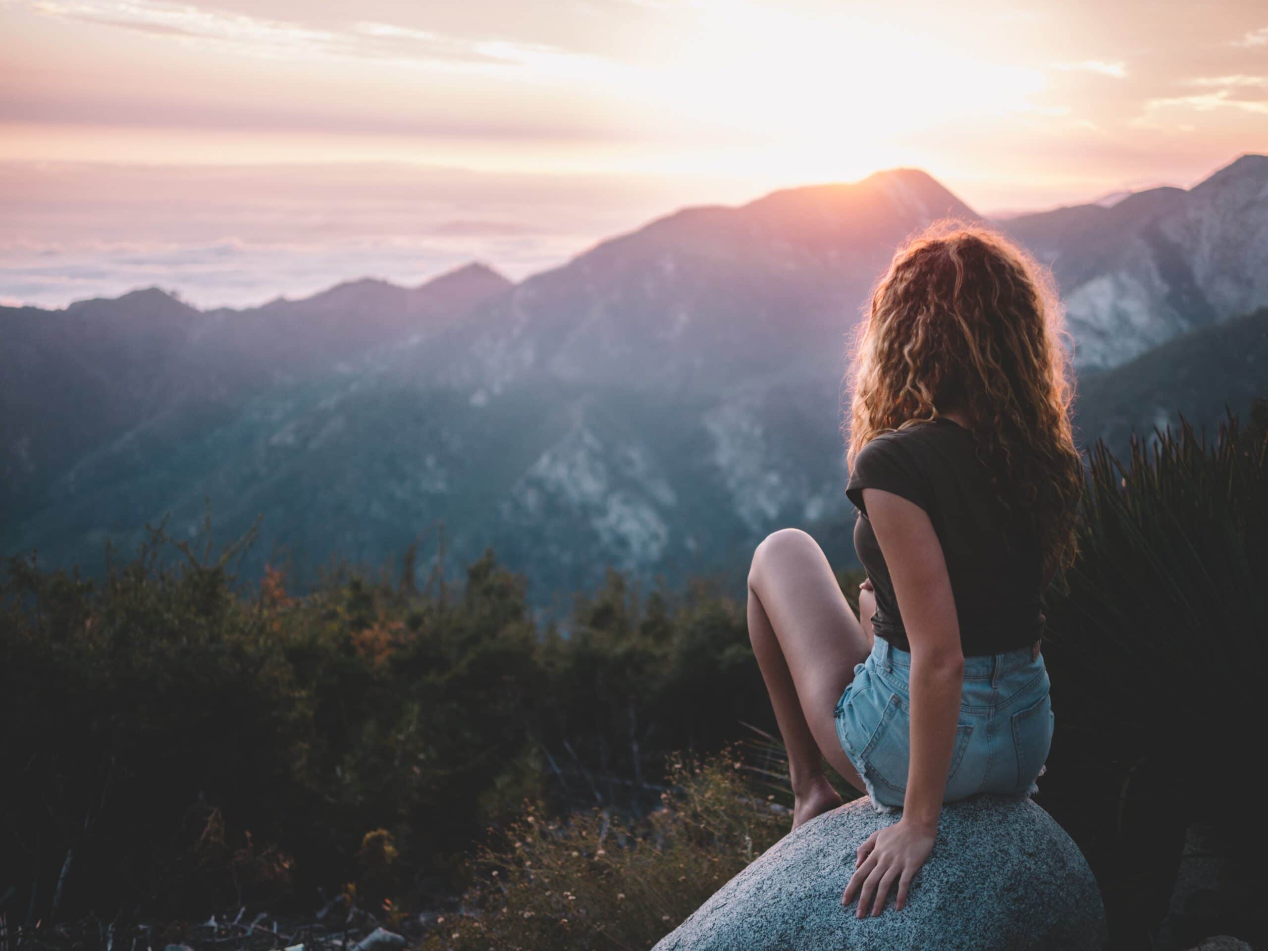 Woman looking over a mountain at sunset