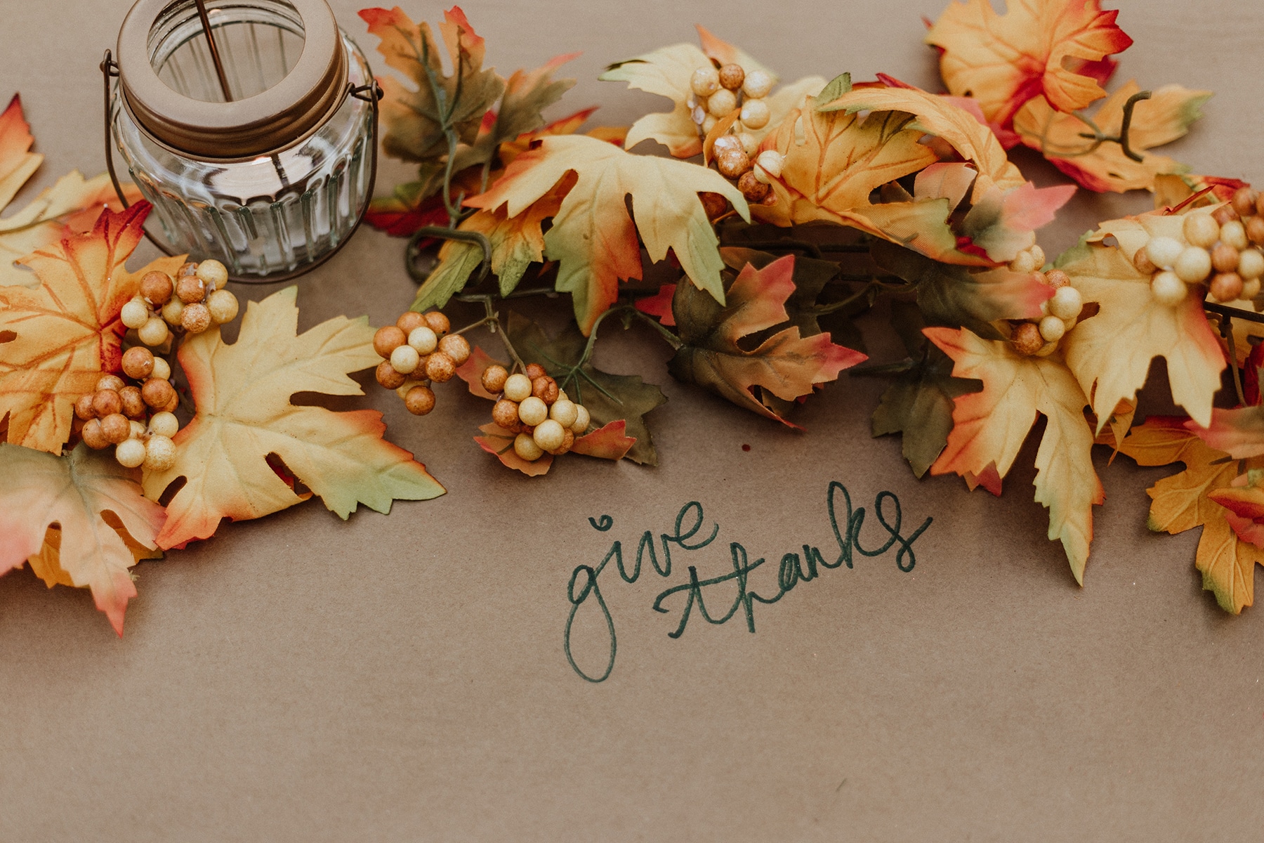 autumn leaves and small candle on brown paper that says give thanks