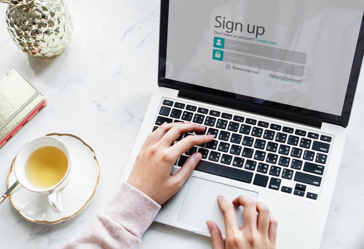 Woman's hands on laptop keyboard next to cup of tea.