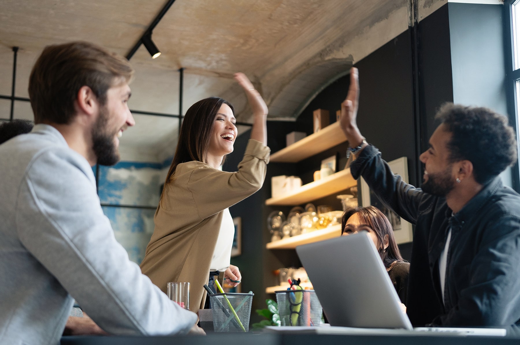 Two cheerful young business people giving high-five while their diverse millennial colleagues looking at them and smiling