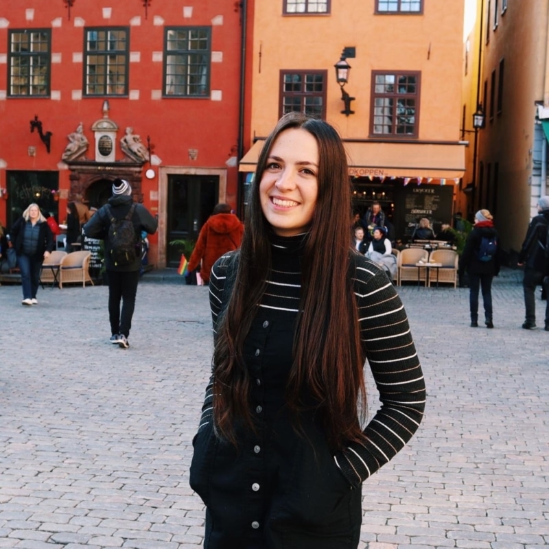 Claire smiling, standing in a picturesque square