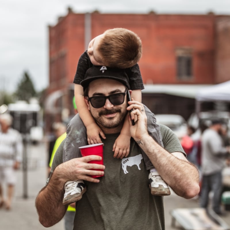 Adam with his child on his shoulders at a street fair