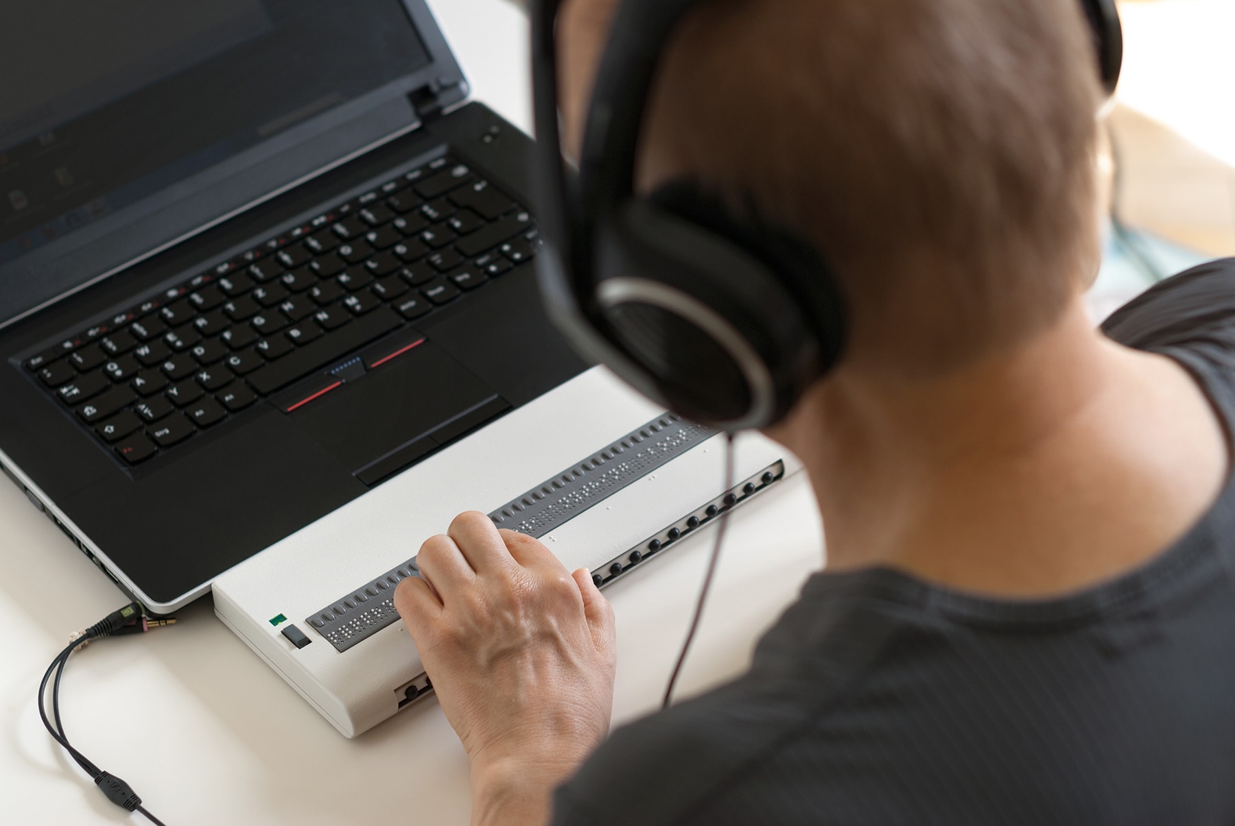 Visually impaired working on computer with assistive technology; braille display and screen reader.