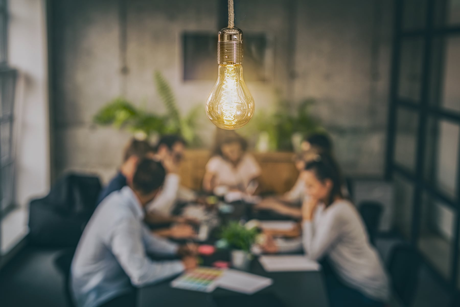 A group of professionals seated around a table meeting with a lightbulb shining brightly overhead