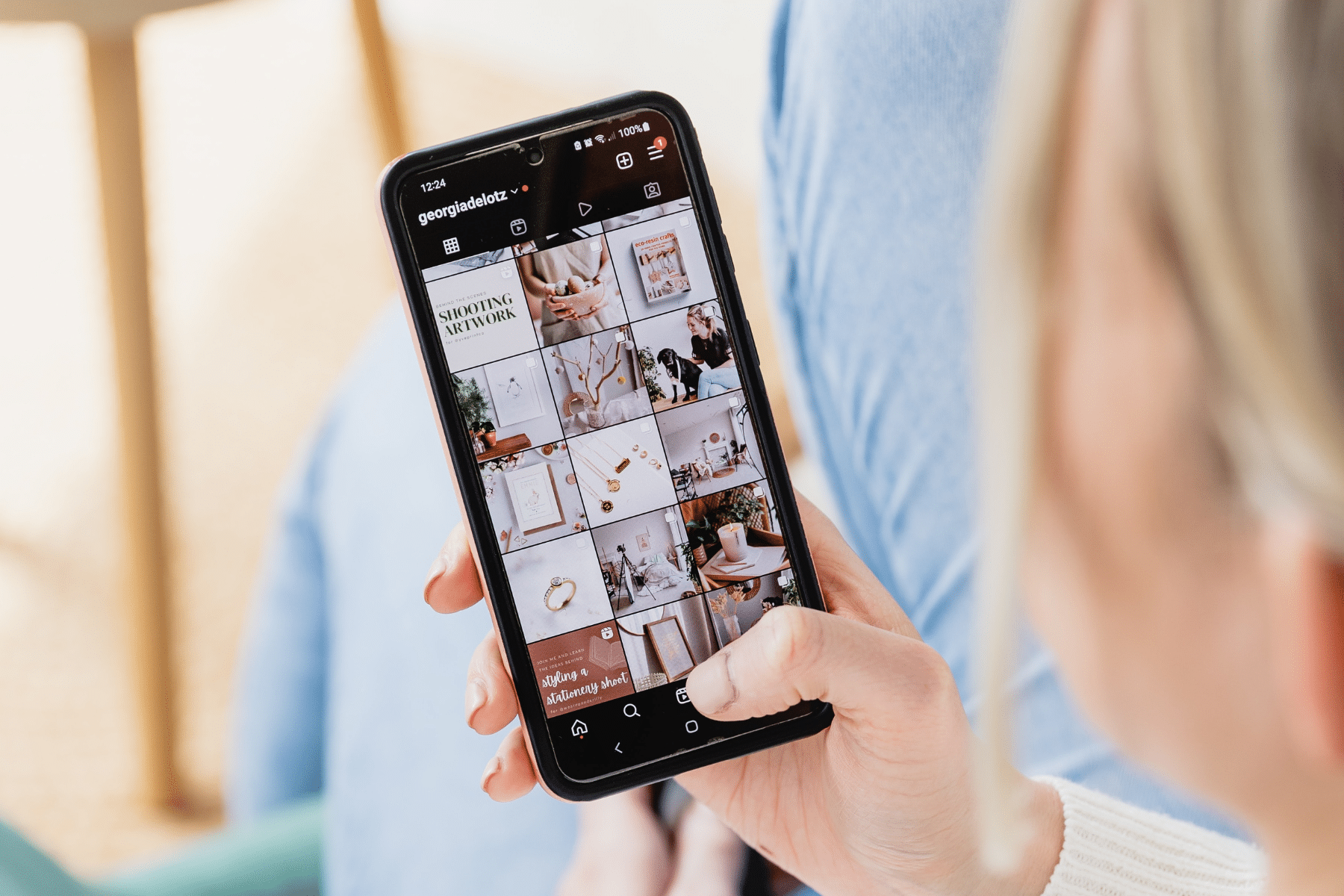 Woman holding phone in hand with phone screen showing Instagram profile grid.
