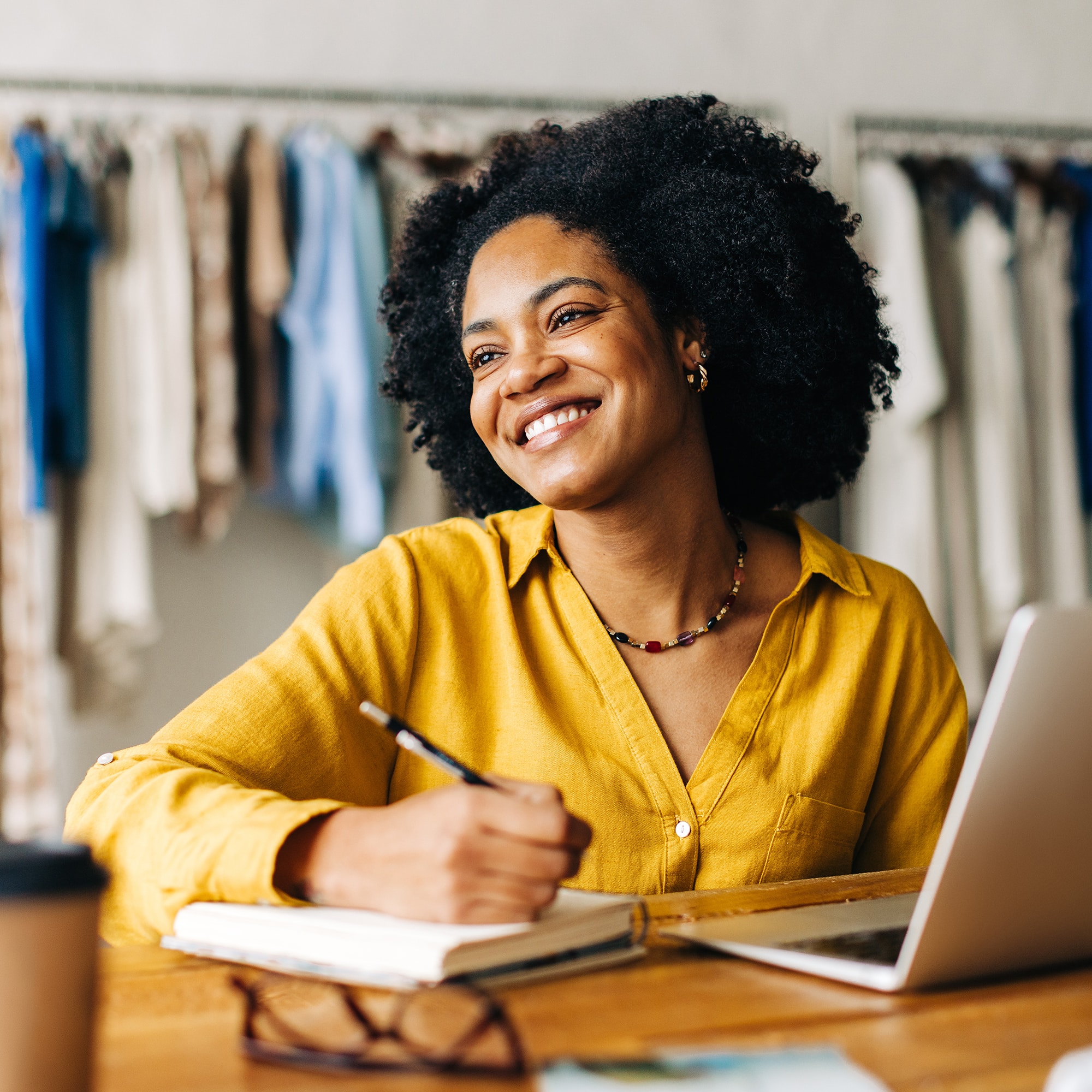 Happy fashion designer smiling confidently as she writes down plans for her small business in a note book